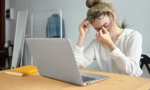 Kobieta w okularach masuje zmęczone oczy przy laptopie.