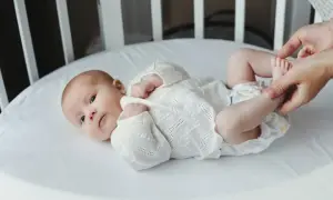 Noworodek w białej koszulce leży w łóżeczku. Dorośli delikatnie dotykają jego stópek. Tak jak widzi noworodek, świat jest rozmazany, ale pełen miłości.