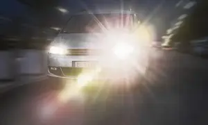 Srebrny samochód jedzie nocą, jego reflektory tworzą olśniewający efekt halo.