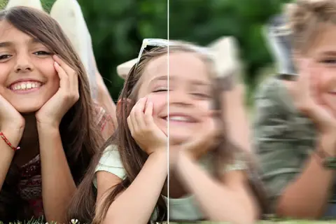 Dwie dziewczynki leżące na trawie, jedna wyraźna, druga rozmazana.