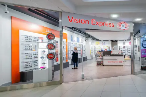 Sklep Vision Express z ekspozycją okularów i kobietą przeglądającą ofertę.