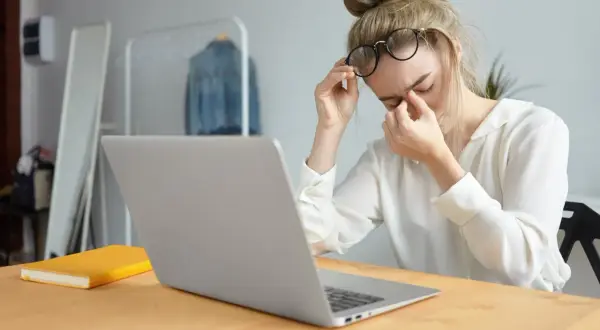 Kobieta w okularach masuje zmęczone oczy przy laptopie.