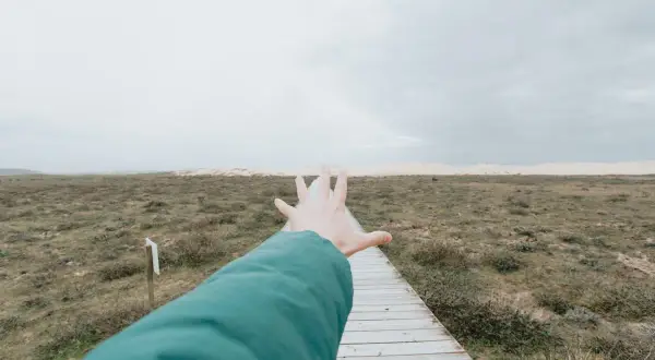 Ręka wyciągnięta w kierunku ścieżki, tworząc wrażenie **widzenia tunelowego** na tle krajobrazu.