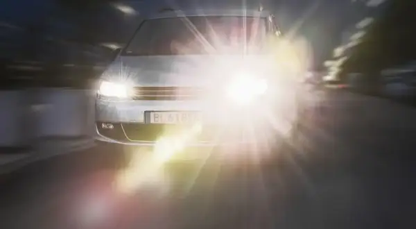 Srebrny samochód jedzie nocą, jego reflektory tworzą olśniewający efekt halo.