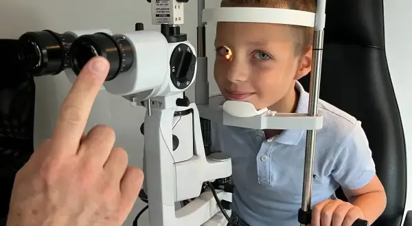 Chłopiec podczas badania okulistycznego. Lekarz sprawdza reakcję źrenic na światło, co może pomóc w diagnostyce.
