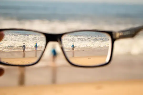 Okulary korygujące widzenie na plaży z dwojgiem dzieci w tle.