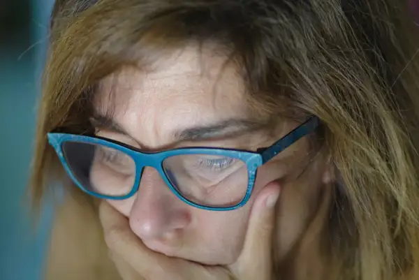 Zbliżenie na twarz kobiety w okularach, z dłonią podtrzymującą podbródek.