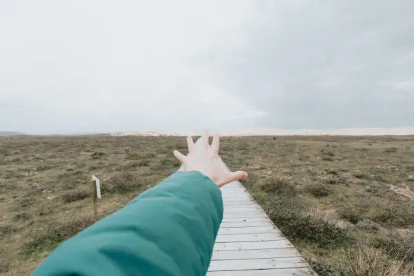 Ręka wyciągnięta w kierunku ścieżki, tworząc wrażenie **widzenia tunelowego** na tle krajobrazu.