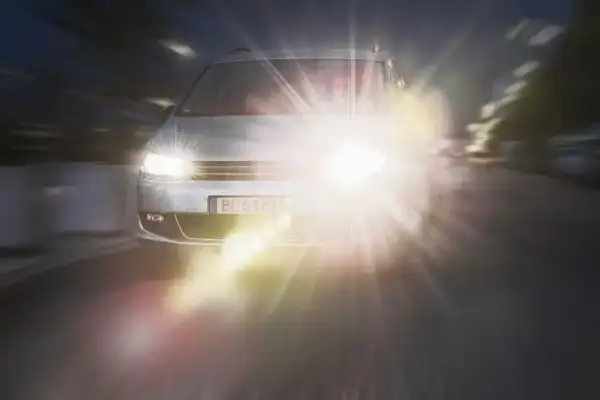 Srebrny samochód jedzie nocą, jego reflektory tworzą olśniewający efekt halo.